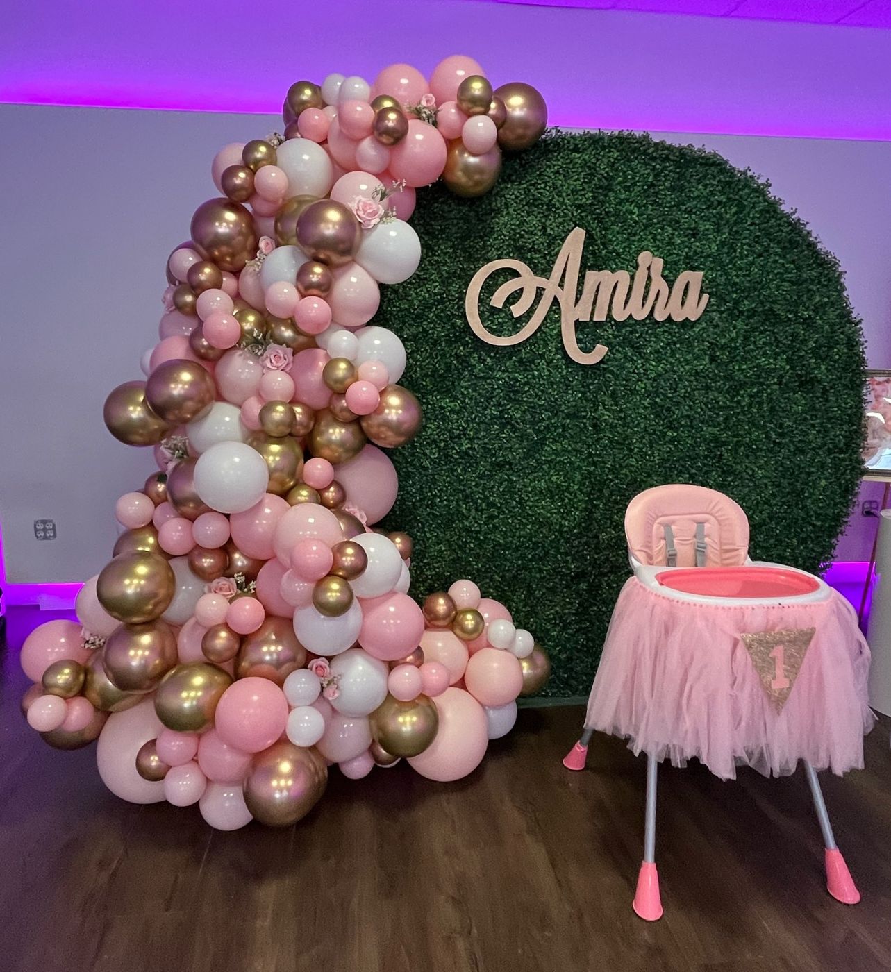 Blush and rose-gold balloon arch on a greenery wall for a private celebration.