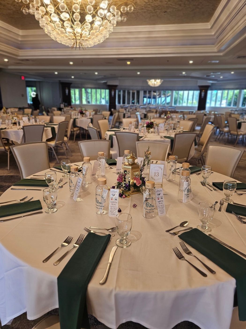 A round reception table with white linens and a gold lantern centerpiece in a ballroom.