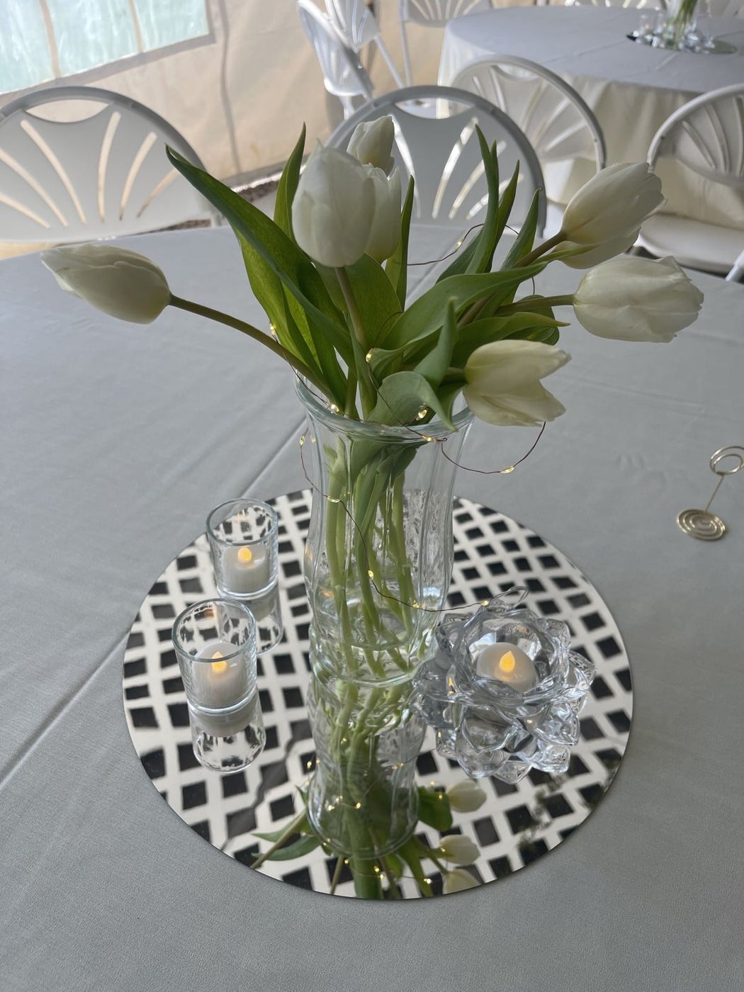 White calla lilies in a glass vase on a mirrored plate with candles.