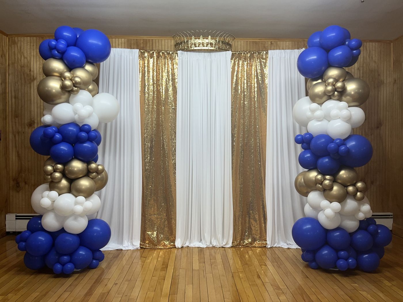 Navy, white, and gold balloon columns beside a sequin drape backdrop.