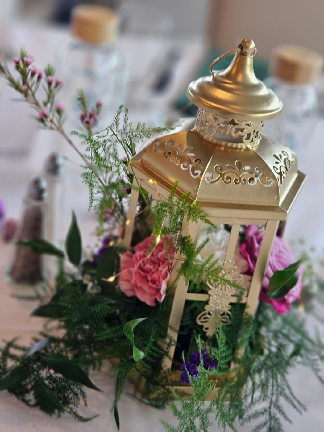 A gold lantern centerpiece with pink florals and greenery on a reception table.