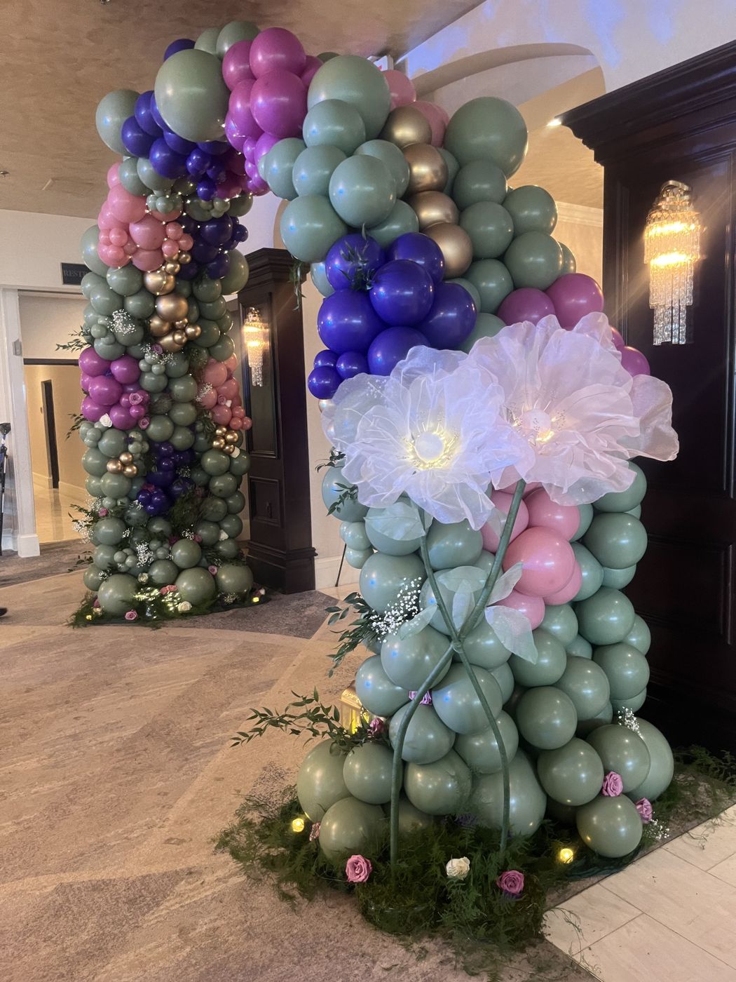 An organic balloon arch in sage, lavender, and blush with an oversized paper flower.